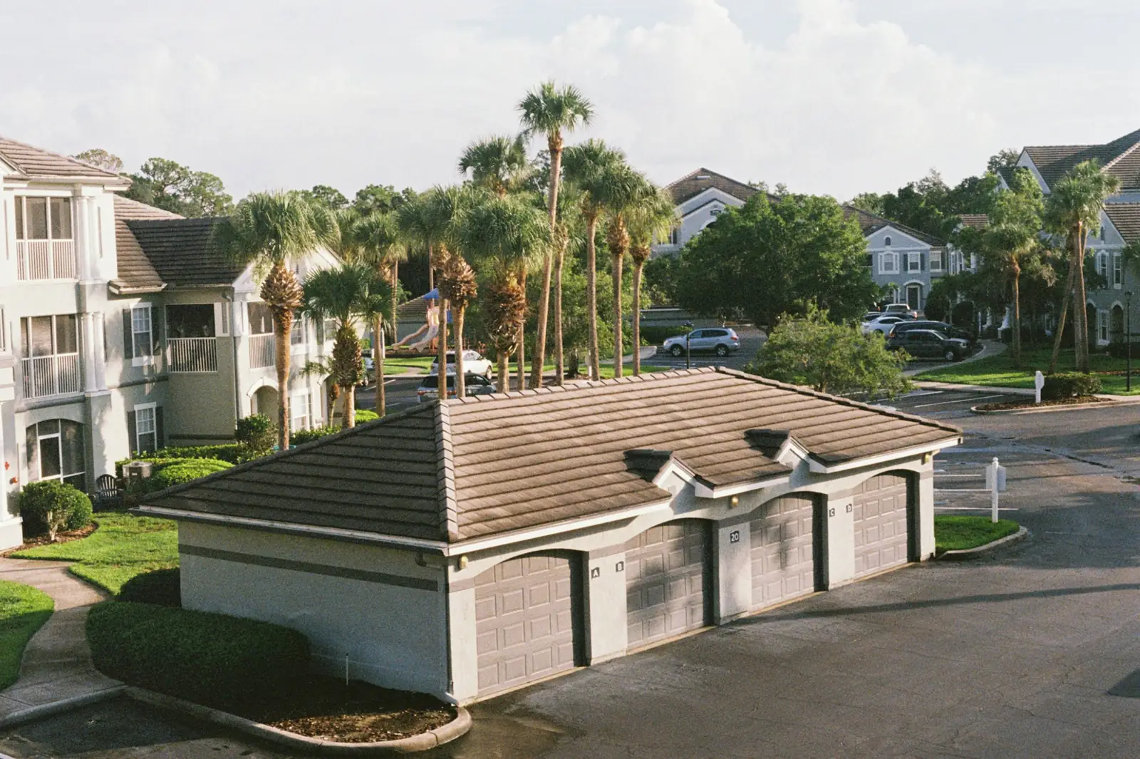A row of garages under a tile roof, with palm trees behind